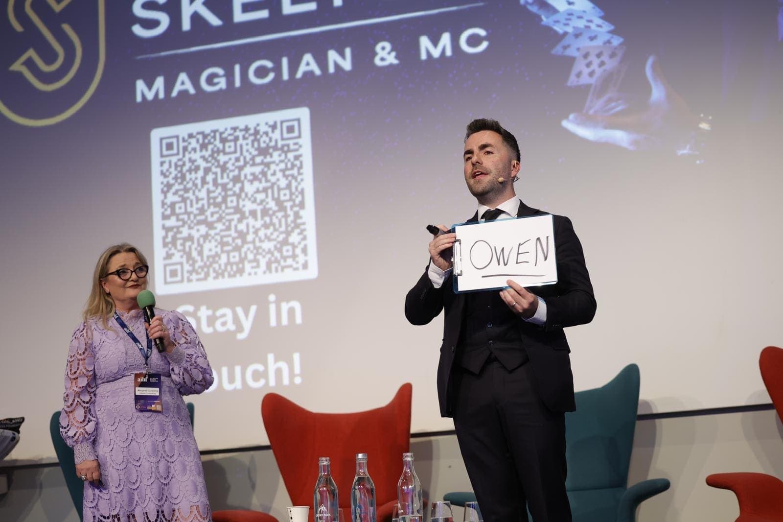 Jamie reveals the name Owen written on a pad beside a delegate with a microphone and lanyard