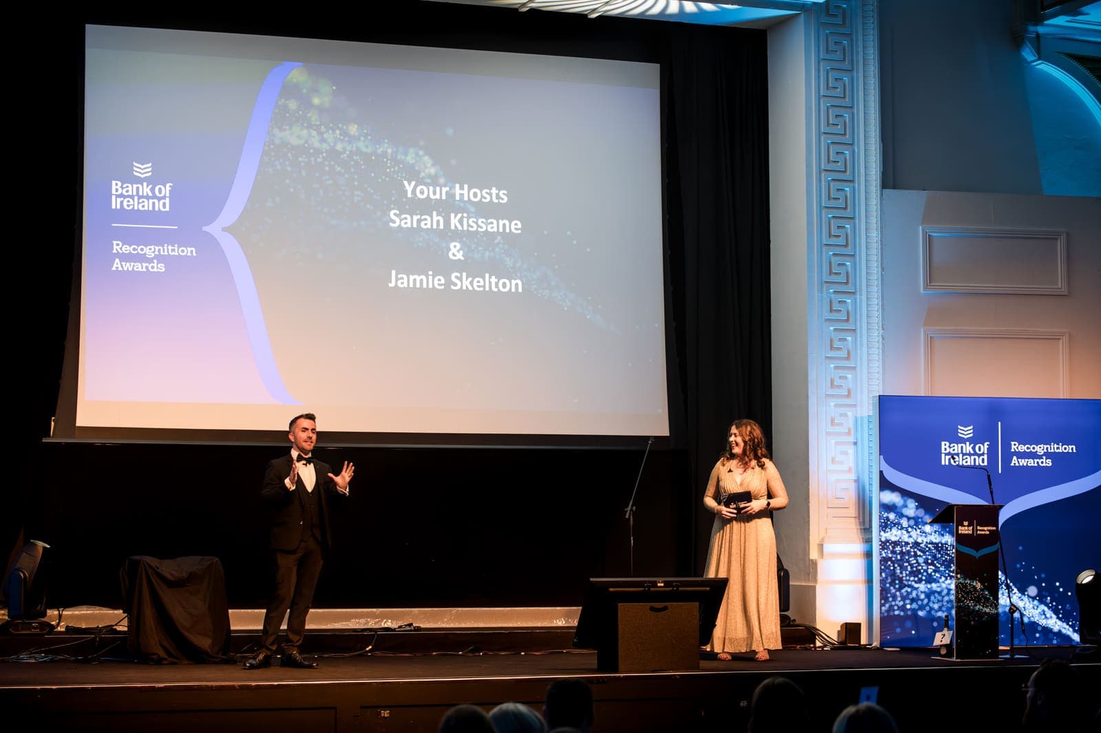 Jamie and co-host Sarah Kissane on stage under a screen that names them as the hosts