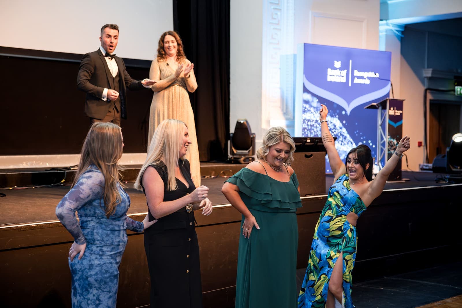 Four women volunteers cheer on the Bank of Ireland awards stage while Jamie watches