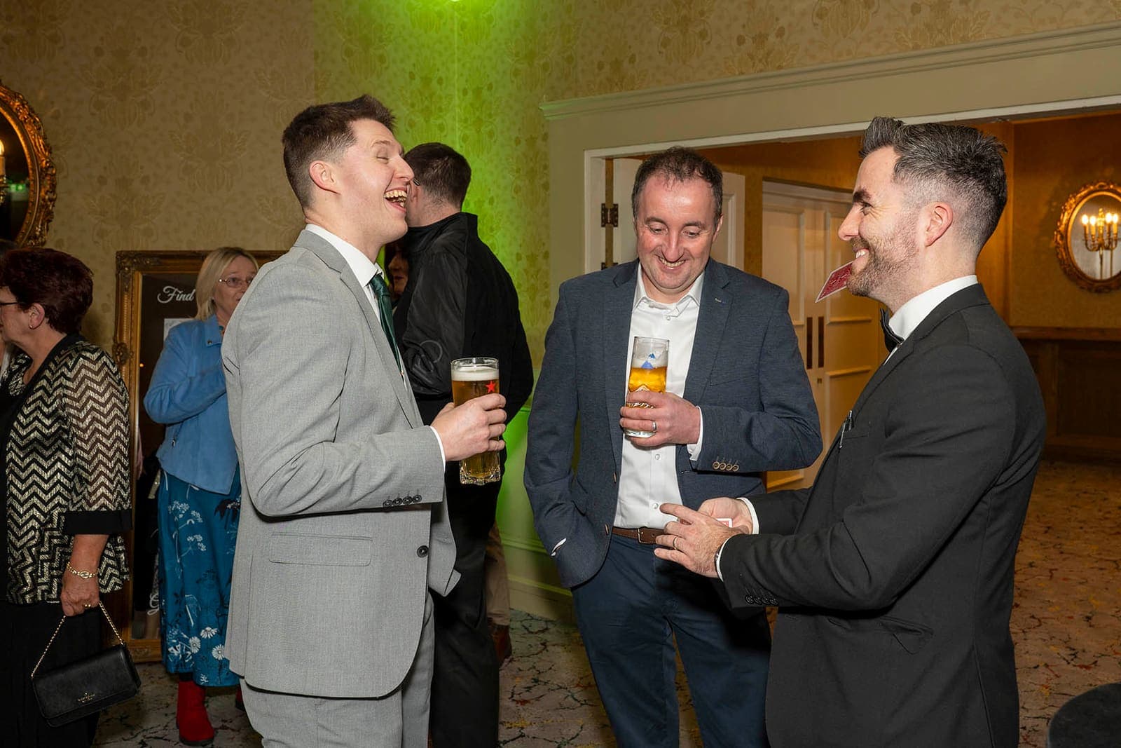 Two men with pints laugh as Jamie performs for them at the drinks reception