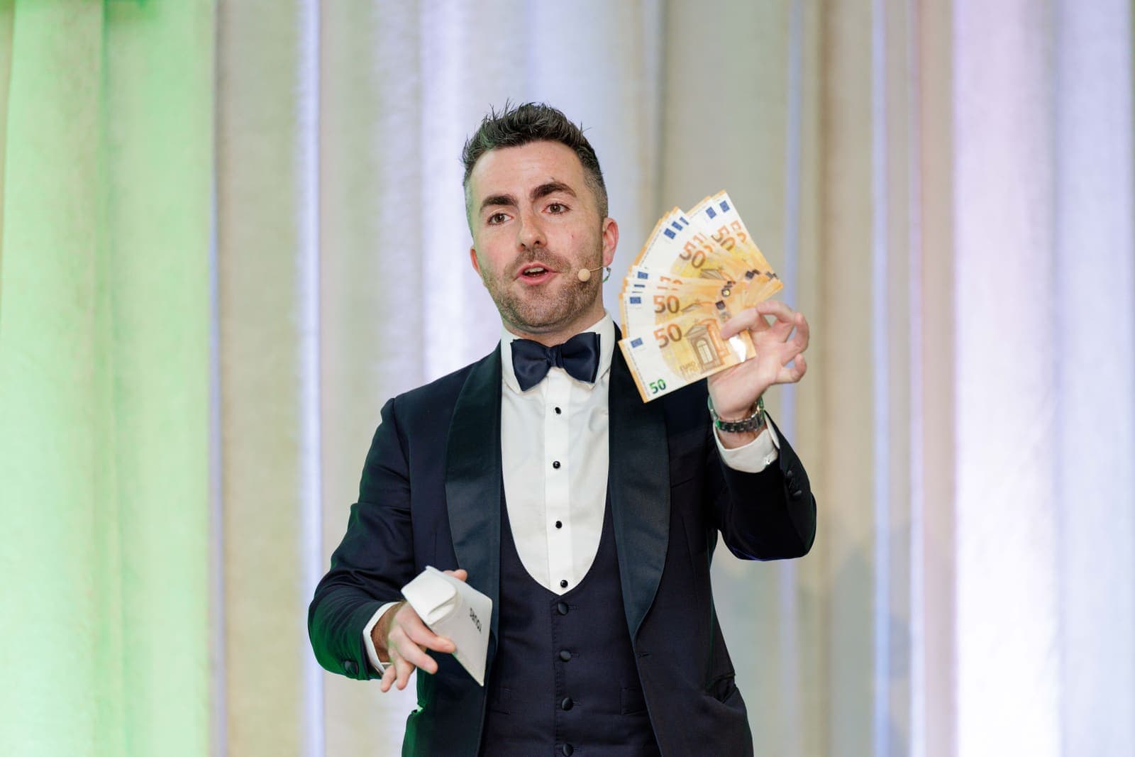 Jamie fans a handful of euro banknotes on the green-lit stage, a card in his other hand