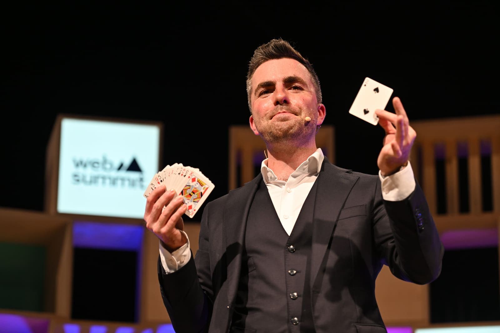 On the Web Summit stage, Jamie fans a deck in one hand and flicks a card into the air with the other