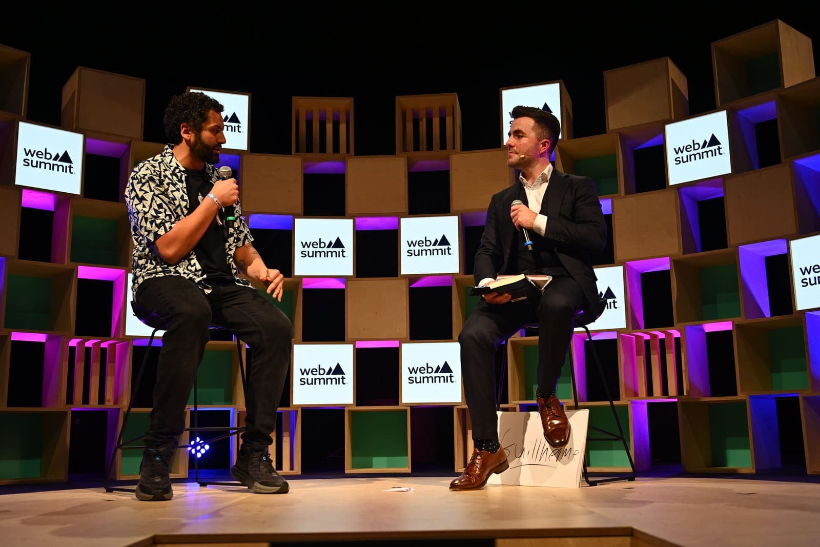 Jamie, microphone in hand, interviews a speaker in armchairs on the Web Summit stage