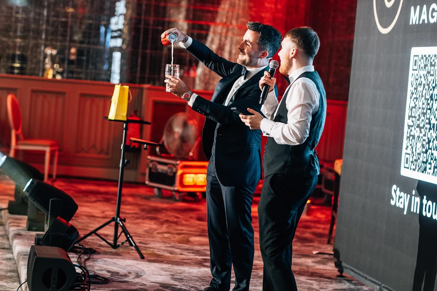 Jamie pours a can into a glass on stage at the Wedding Help Northern Ireland Awards 2025 beside a guest with a microphone