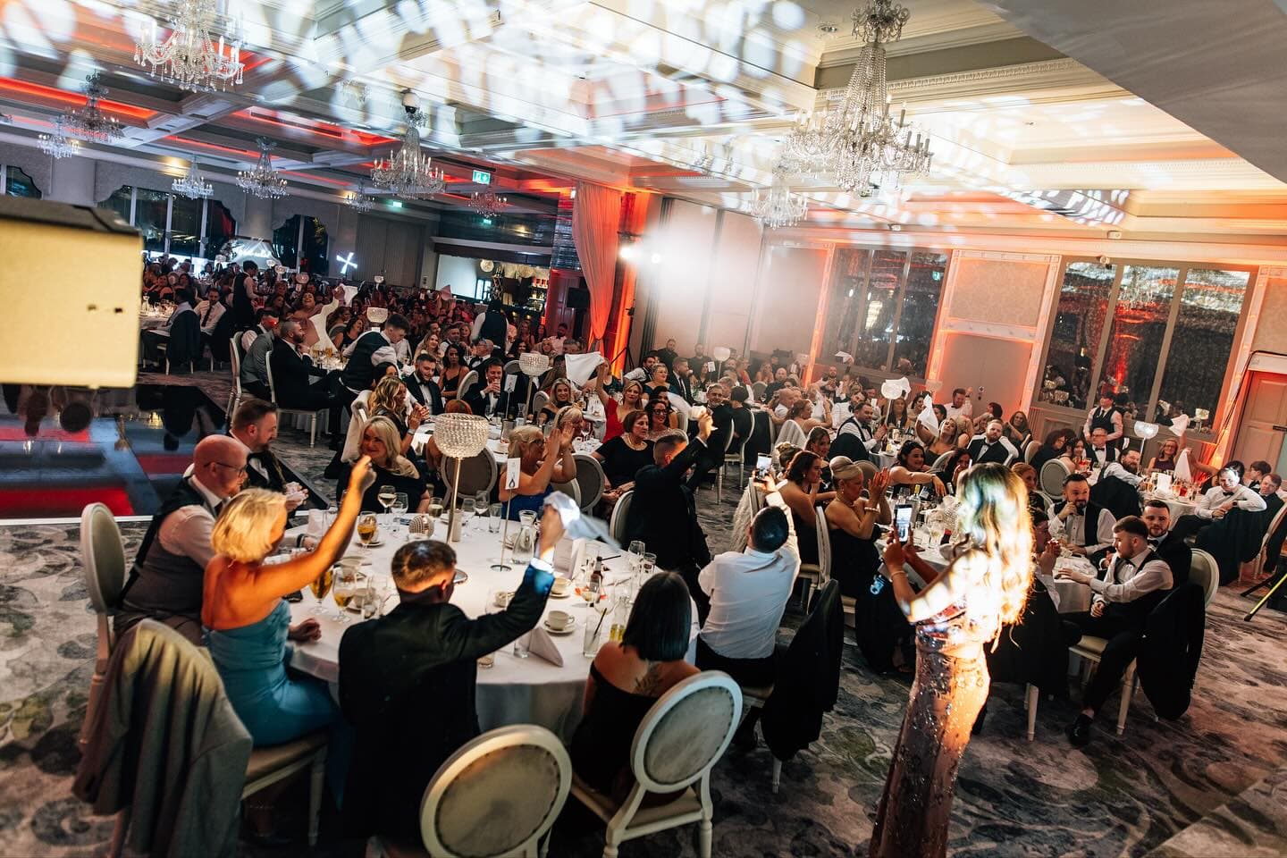 A full ballroom of guests at the Wedding Help Northern Ireland Awards 2025 cheer and wave napkins at their tables