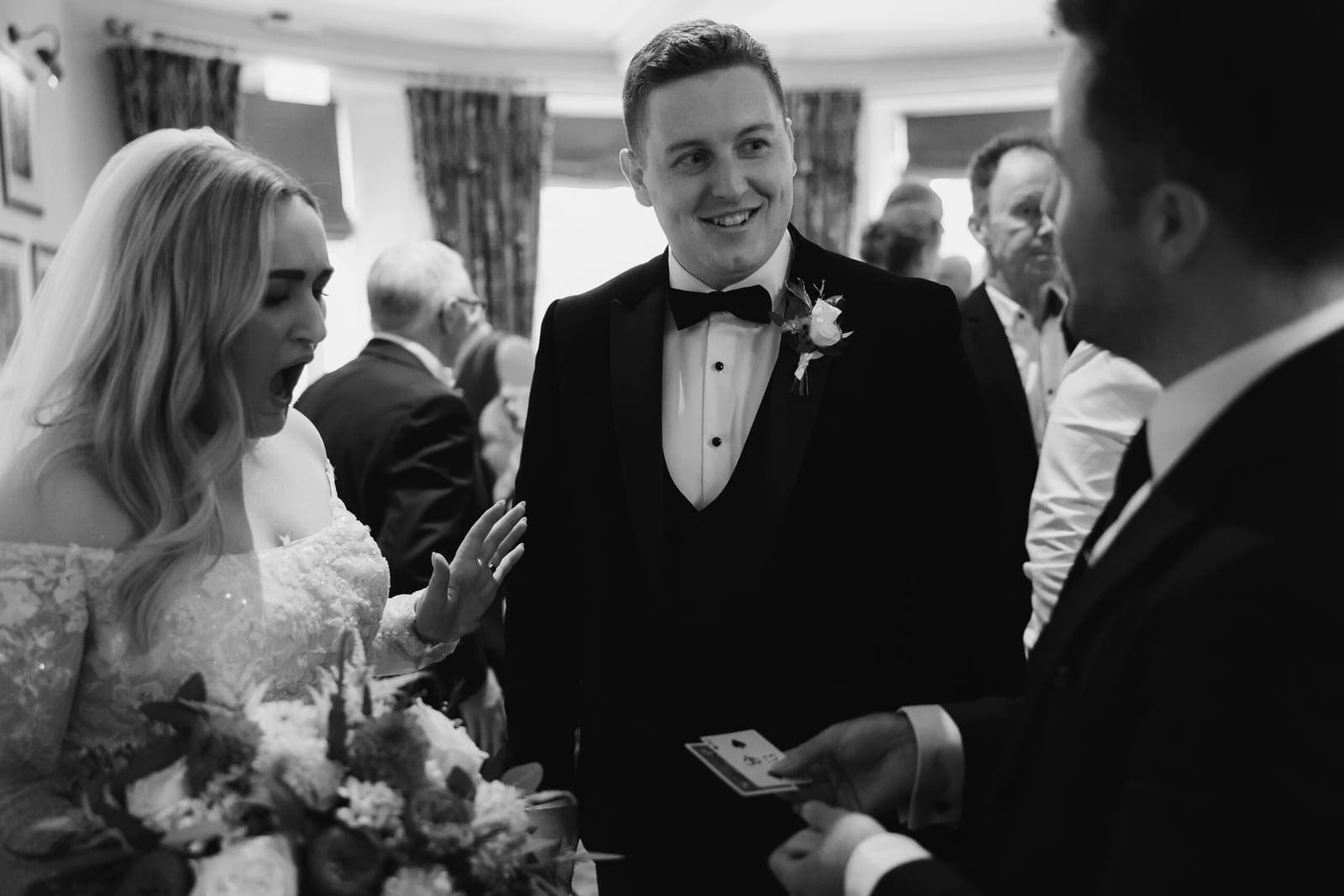 Black-and-white: card trick for a bride and groom with guests behind
