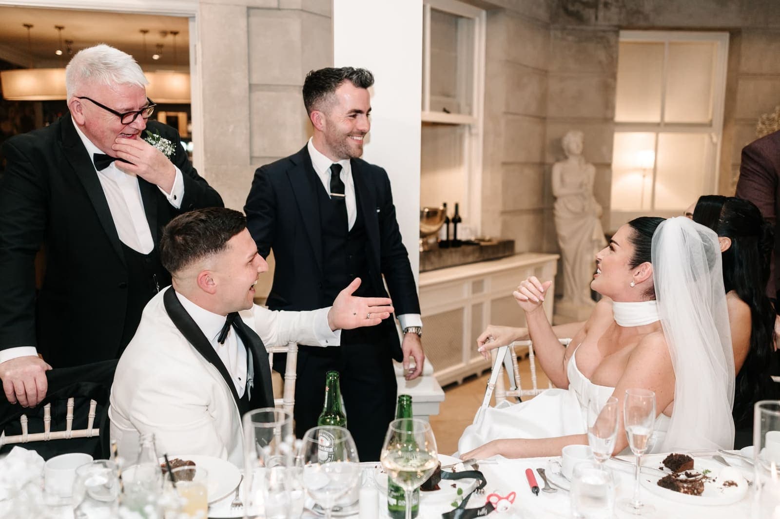 A groom in a white tuxedo jacket and the bride laugh at a trick at the top table