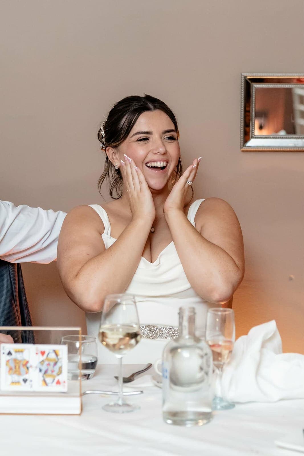 A bride at her table laughs with both hands on her cheeks