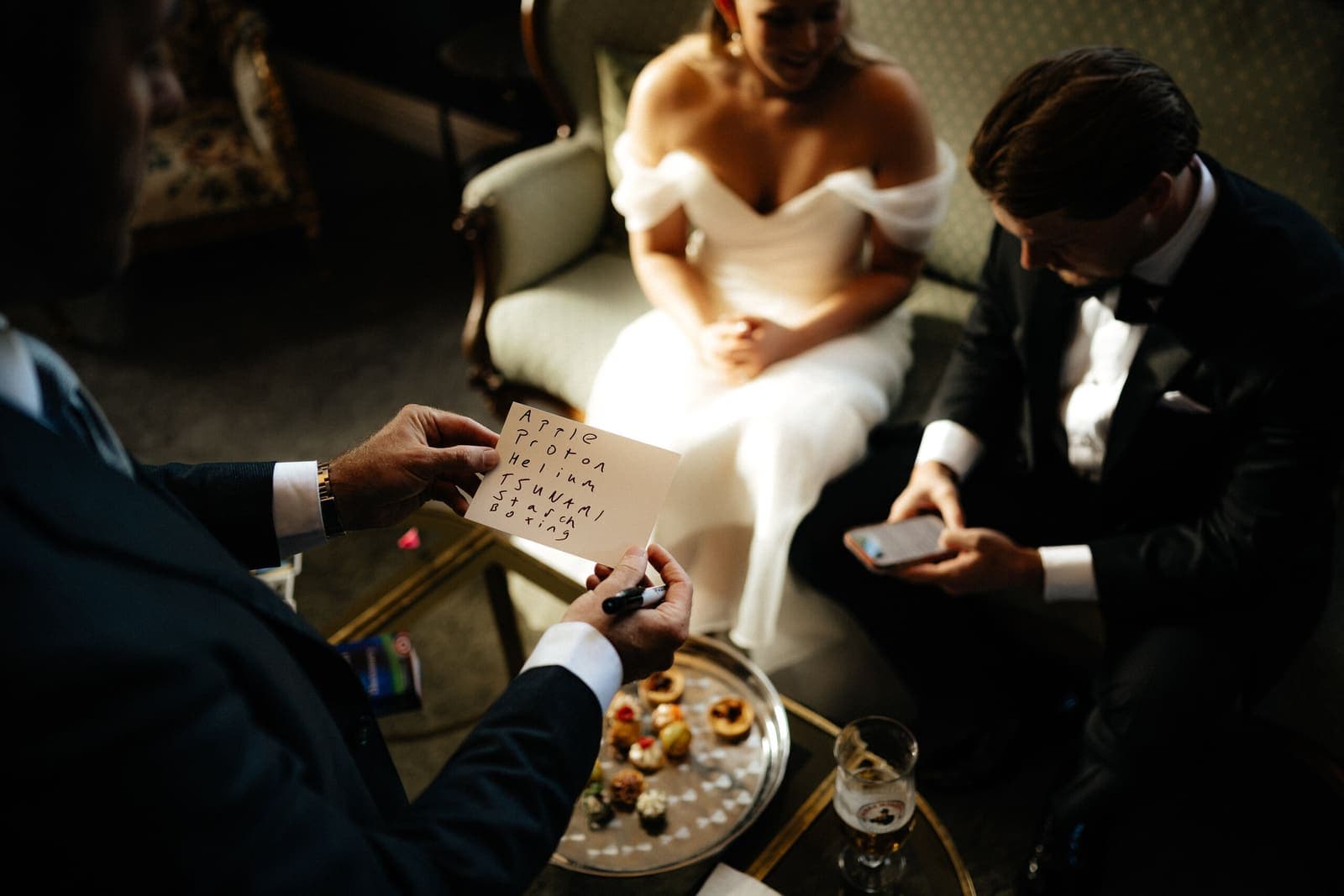 Bride on a sofa watches a card trick; warm low light