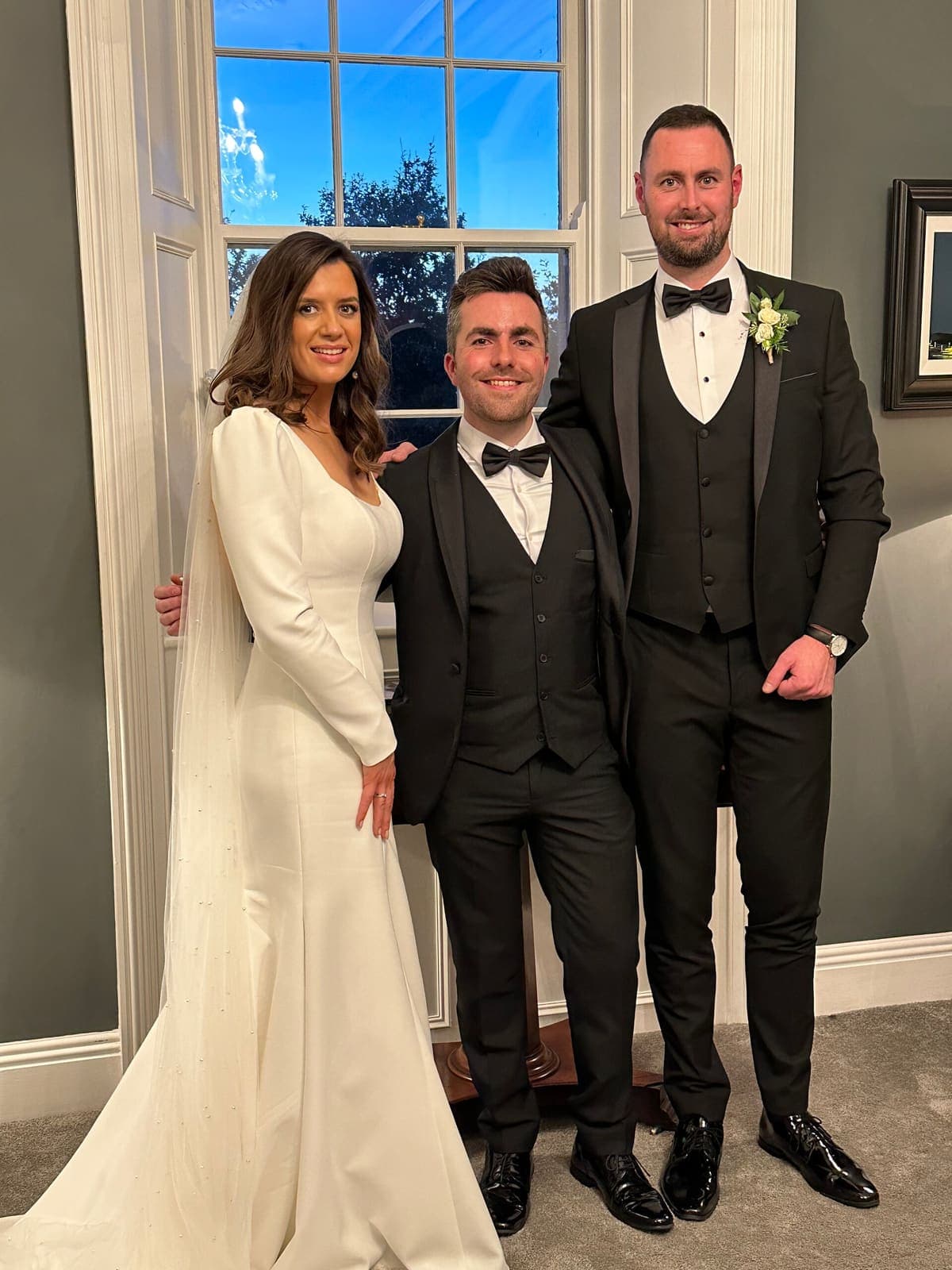 Bride, groom and Jamie posing by a window
