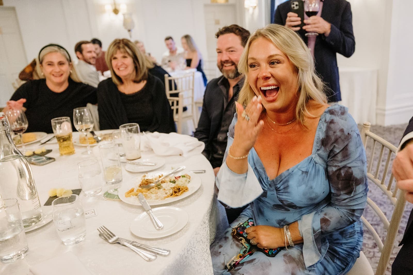 Woman at a dinner table in blue reacts with delight