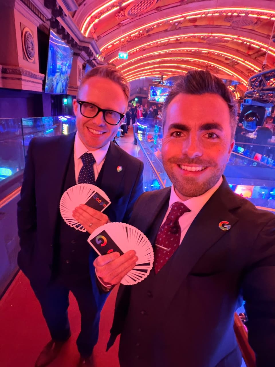 Jamie and a second performer each fan out a deck of cards with Google backs on a balcony above a busy event