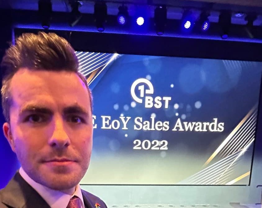 Jamie takes a selfie in front of a stage screen that reads EoY Sales Awards 2022
