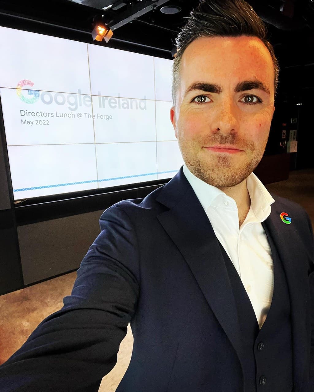 Jamie takes a selfie in front of a wall of screens that reads Google Ireland