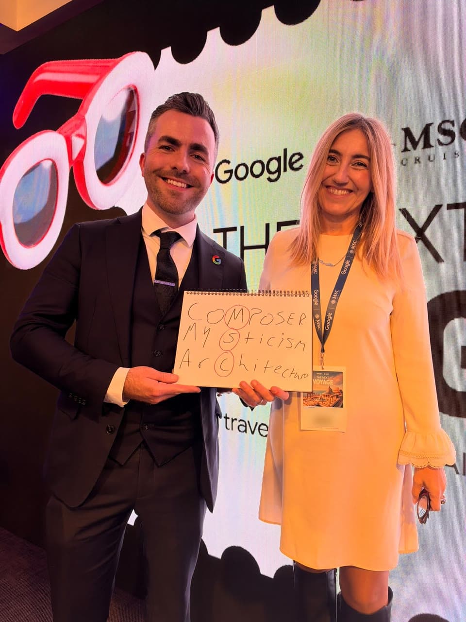 Jamie and a smiling guest hold up a pad with three words and the circled letters M, S and C, in front of a Google and MSC Cruises backdrop