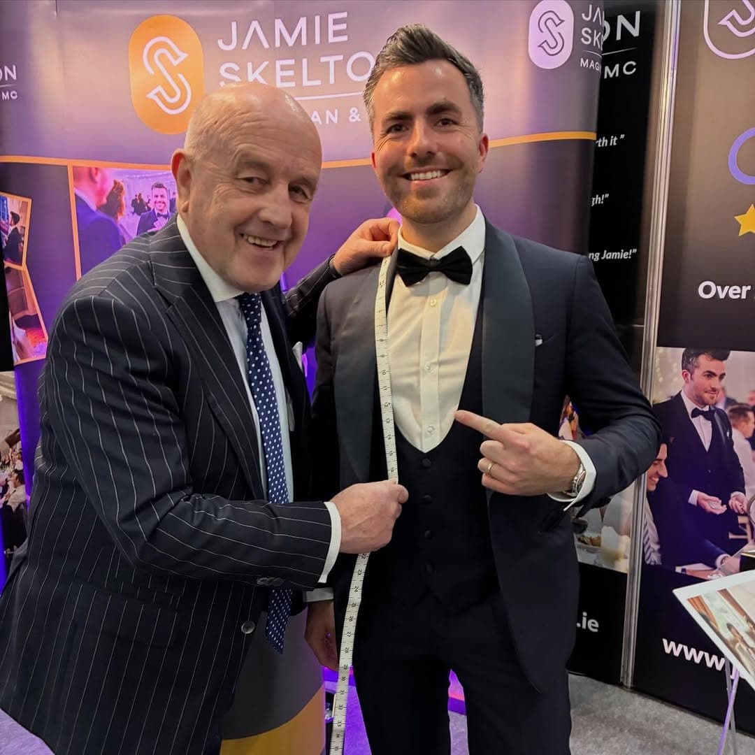 Master tailor Louis Copeland holds a tape measure to Jamie, who smiles in a tuxedo and bow tie at his stand at the RDS wedding show