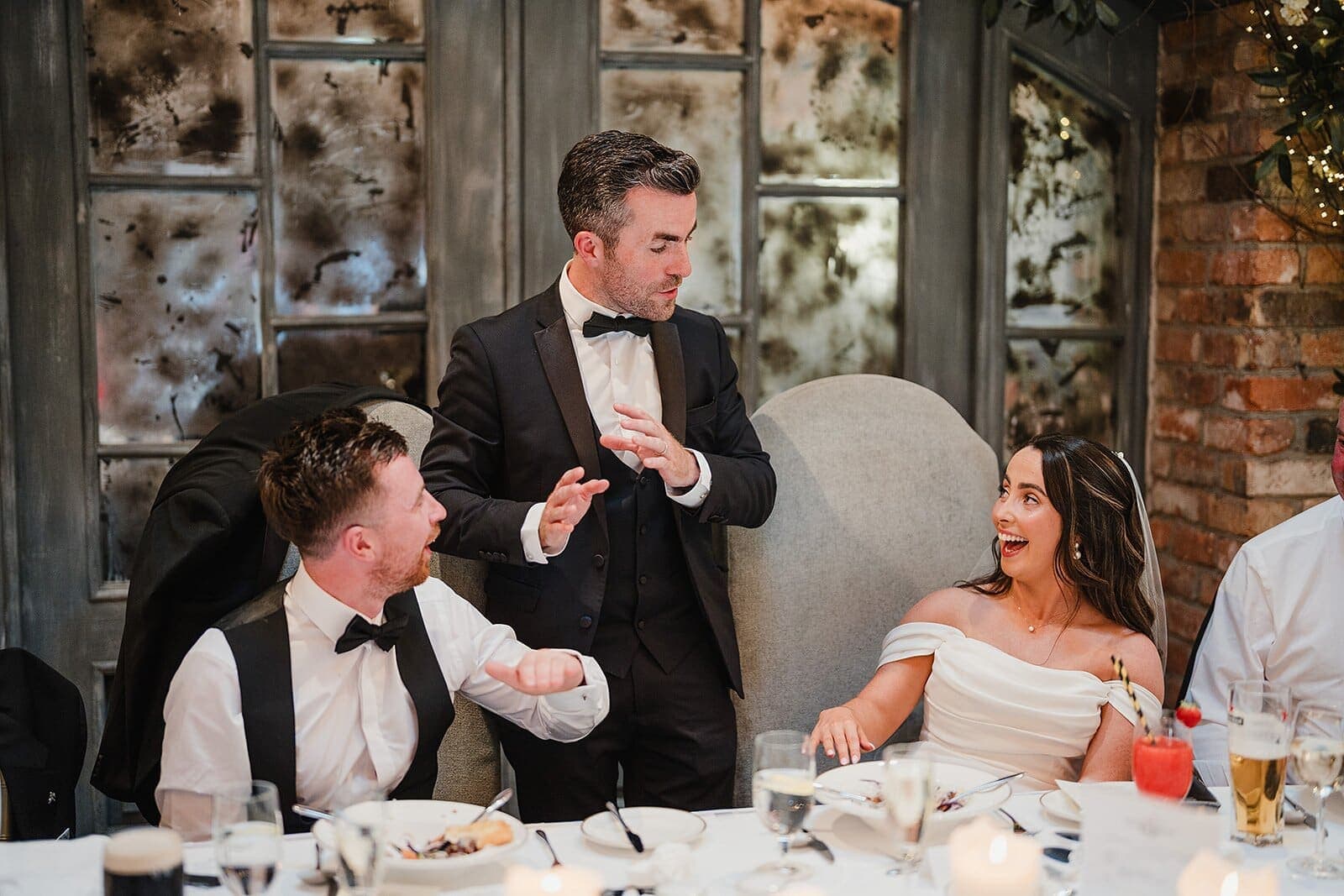 Wedding top table in a rustic room; bride and groom laugh at a trick