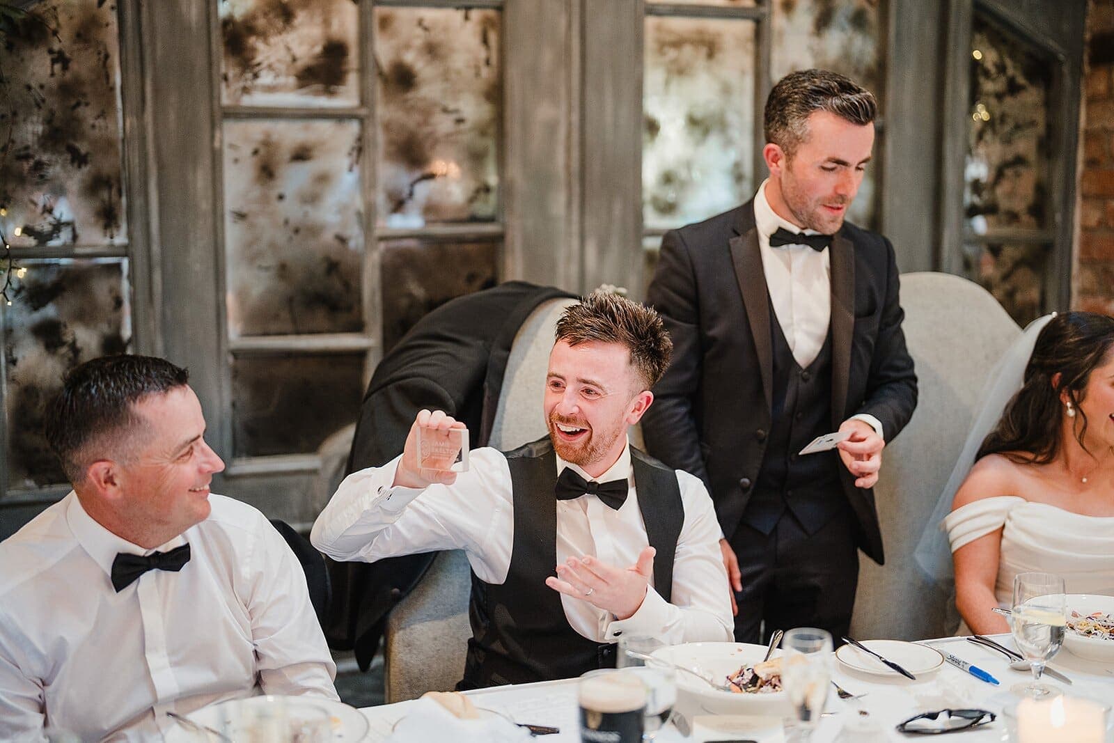 Groomsman at a top table laughs at a trick beside the bride