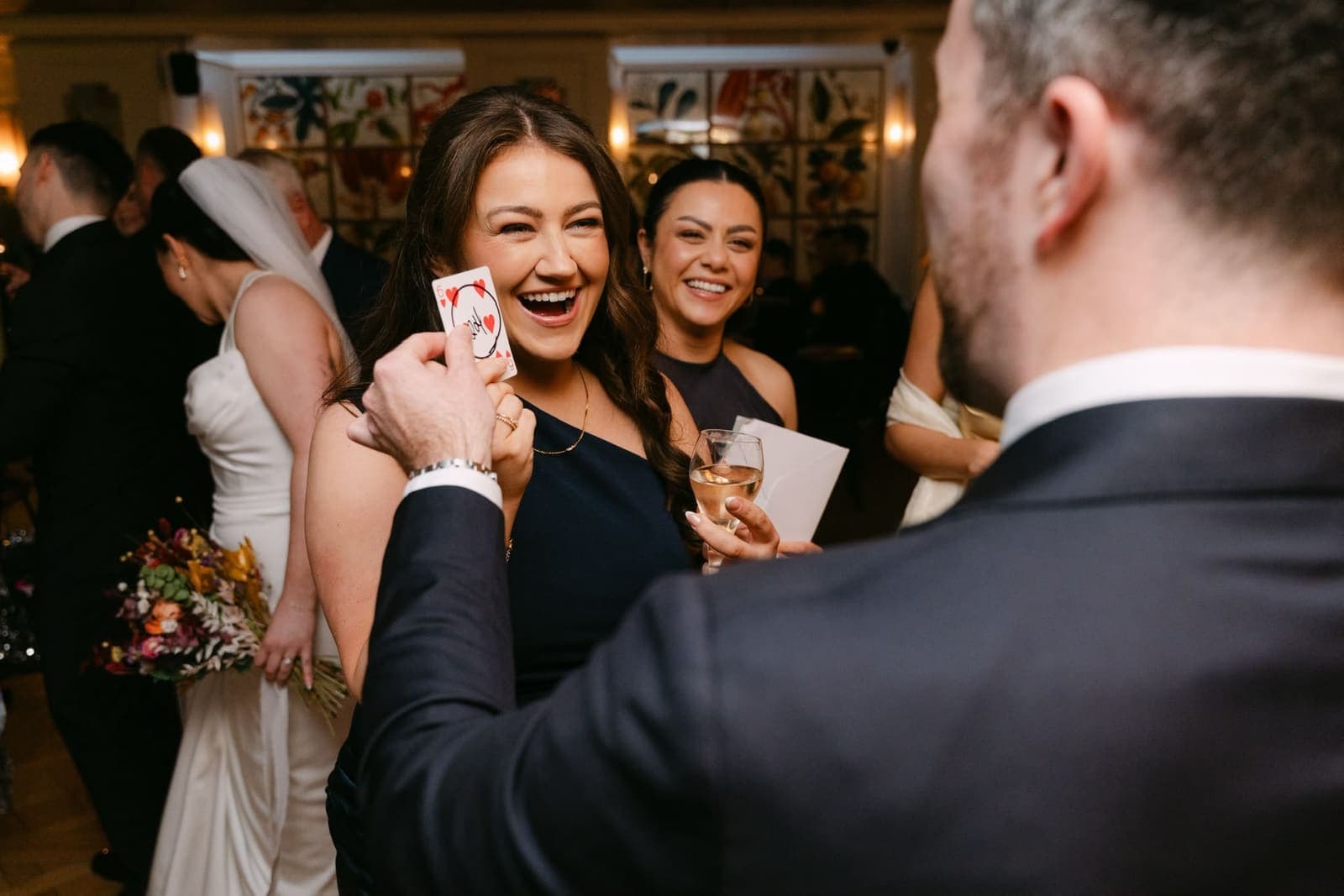 A guest laughs as Jamie holds up her card, with the bride behind her