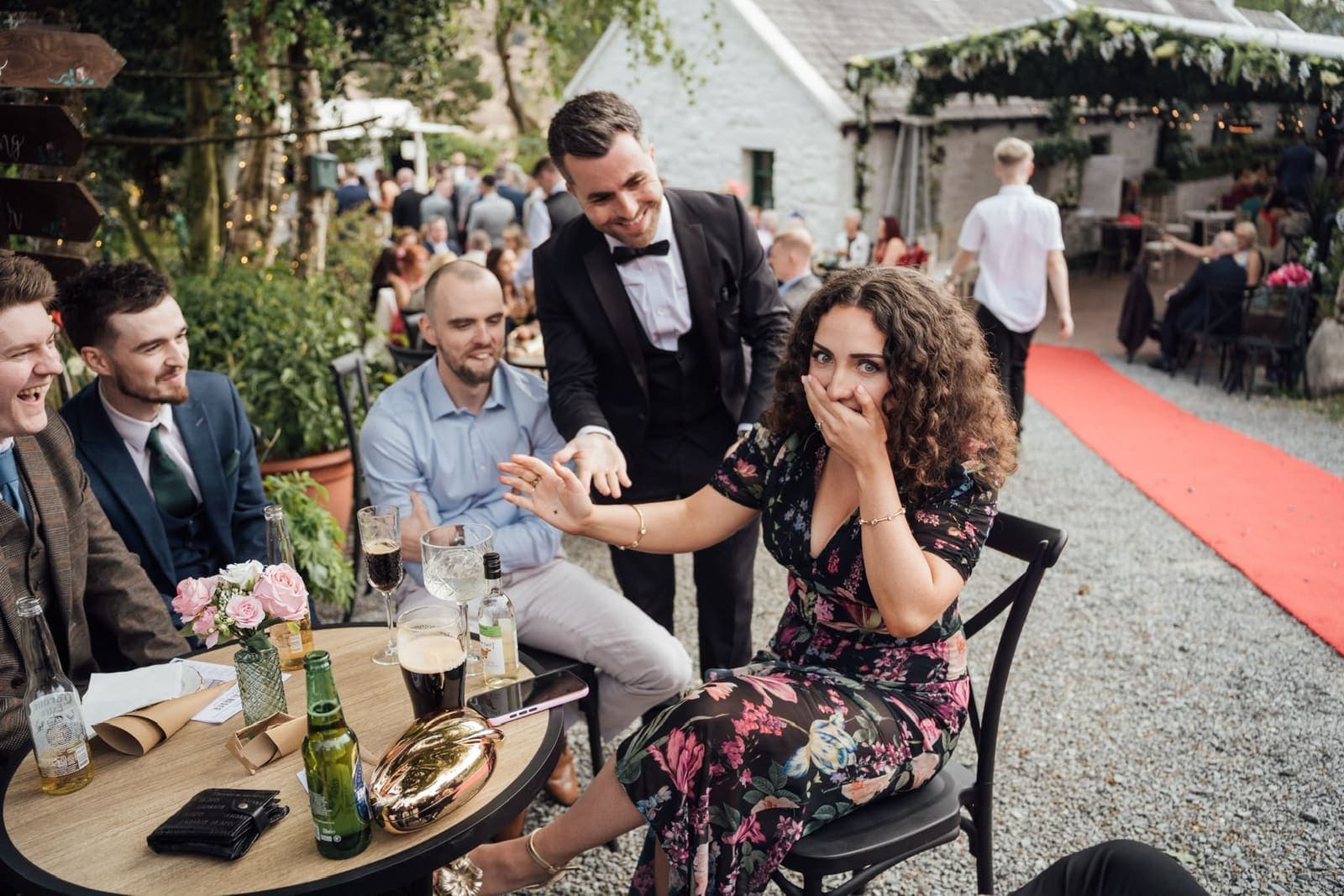 At an outdoor drinks reception, a guest covers her mouth in shock as Jamie finishes a trick