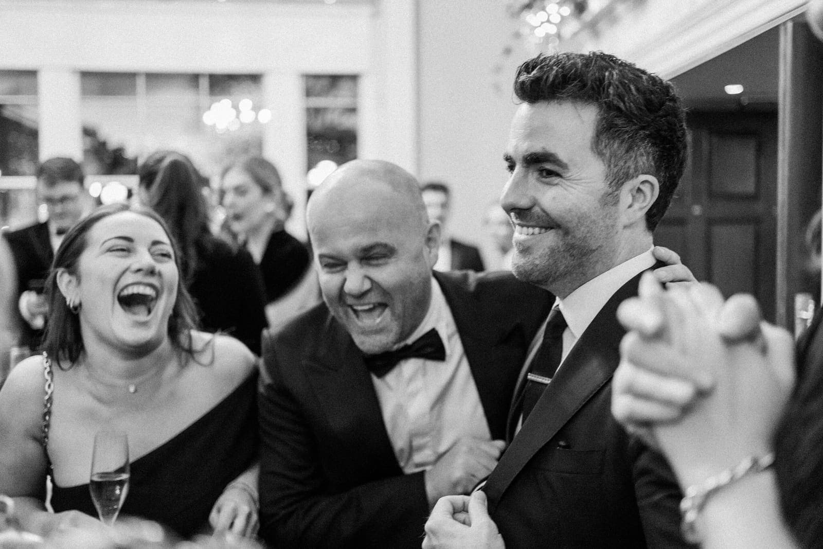 Black-and-white: wedding guests laughing hard during close-up magic