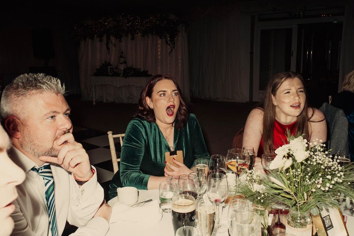 A guest in a green velvet dress gasps at a trick at a wedding dinner table