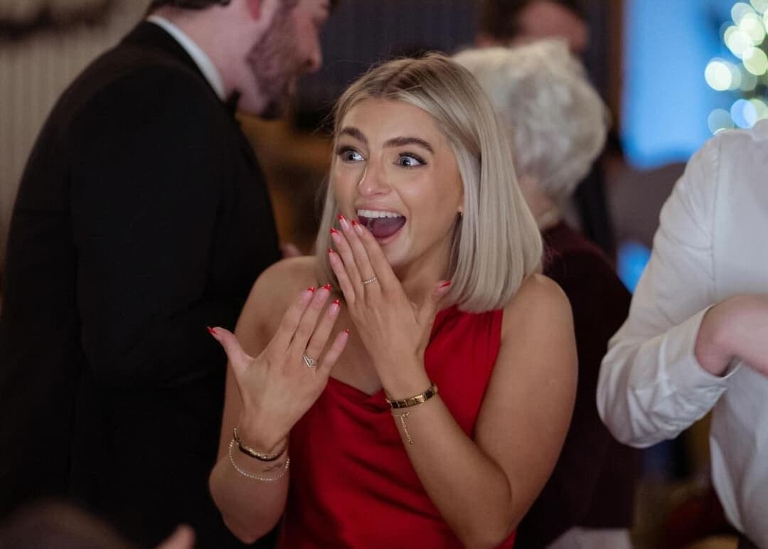 Close-up of a blonde woman in red with hands raised in amazement