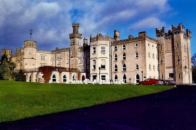 The stone front and towers of Cabra Castle across a green lawn under a blue sky