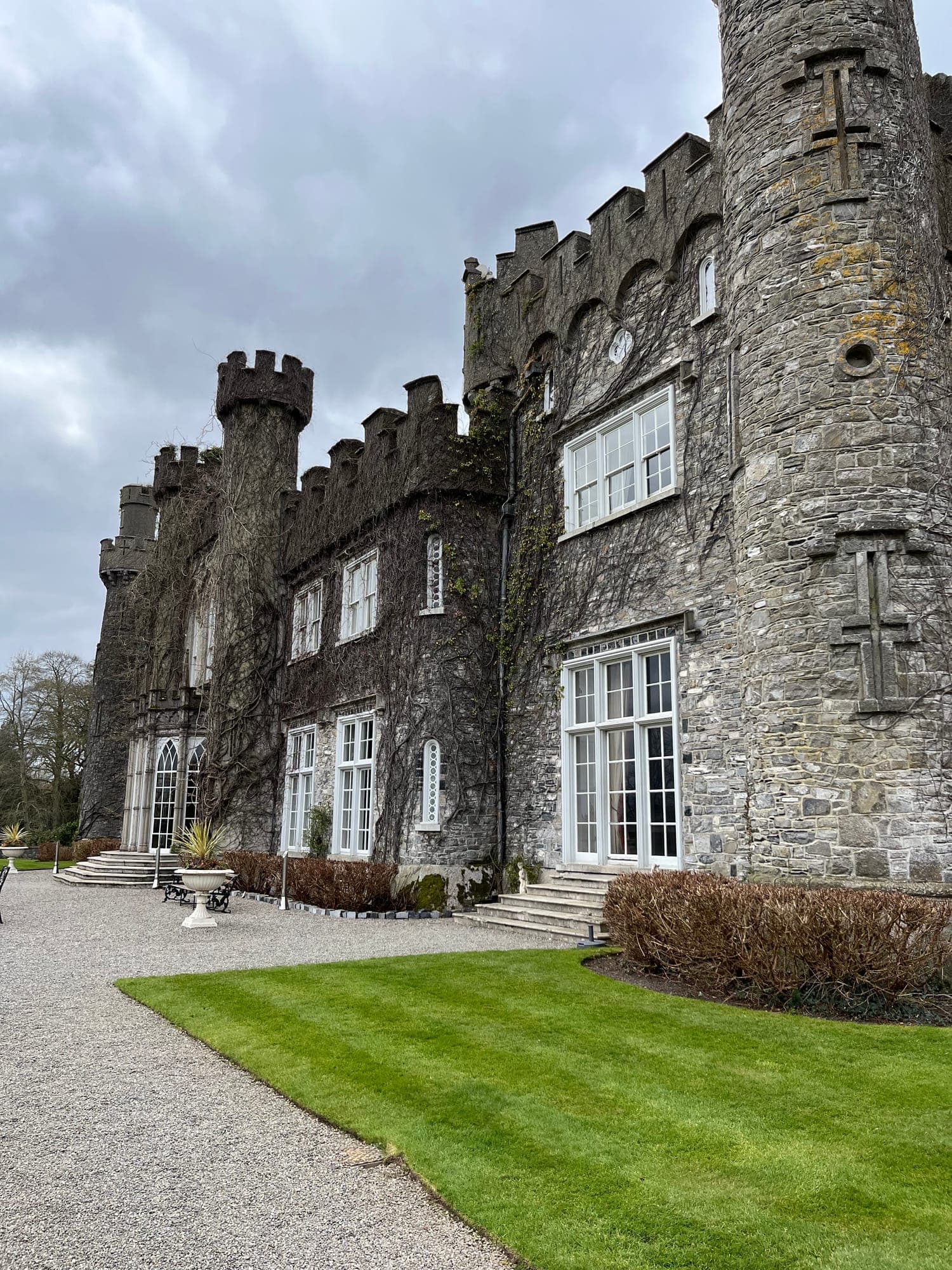 The battlemented Gothic facade and round tower of Luttrellstown Castle above a gravel path and lawn
