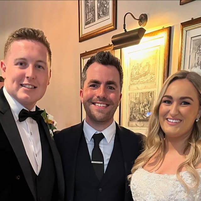 The groom, Jamie and the bride smile together indoors at Jessica and James's wedding at Bellingham Castle