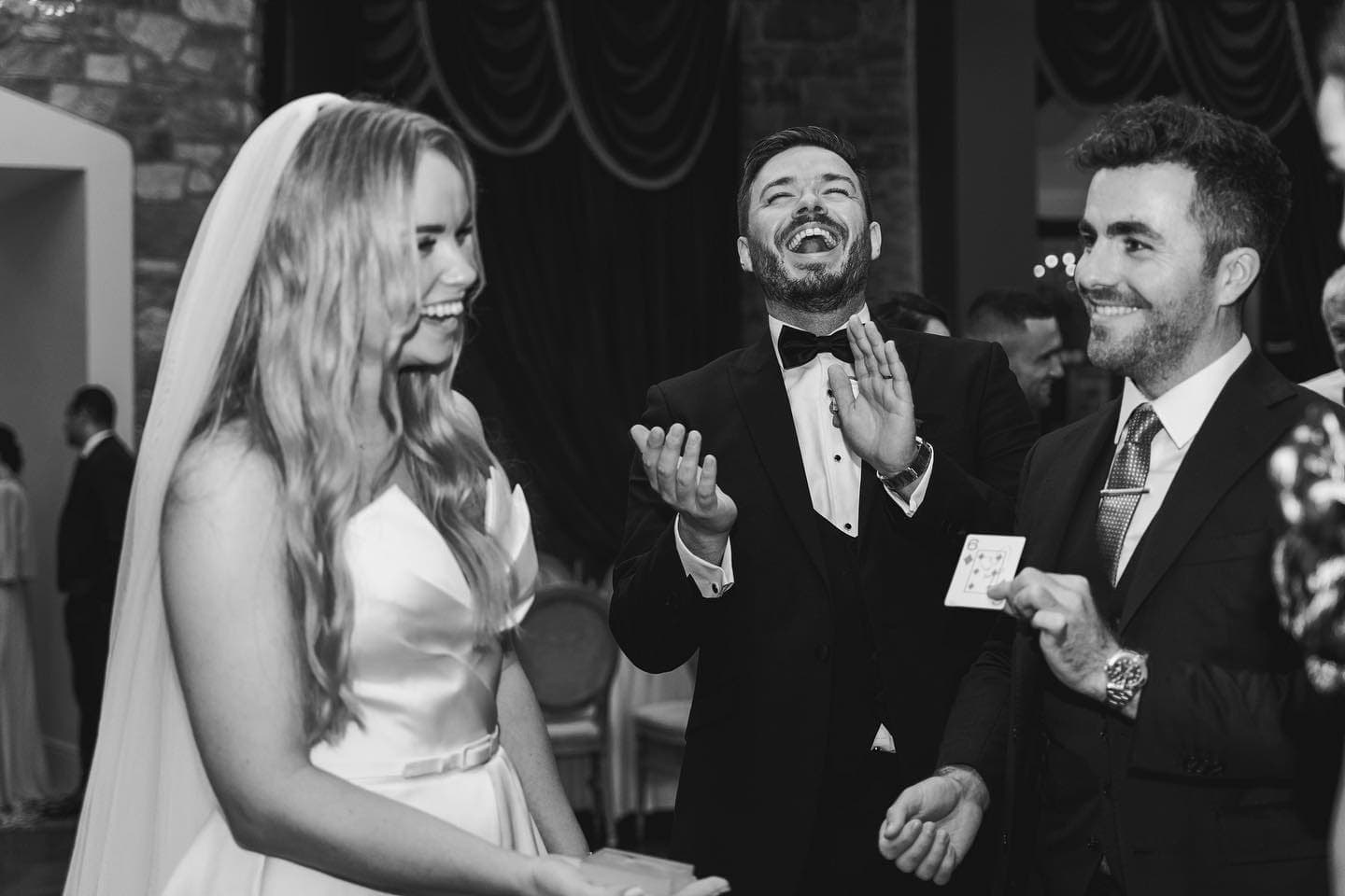 Black and white: at Cabra Castle, the groom throws his head back laughing and the bride smiles as Jamie holds up a card