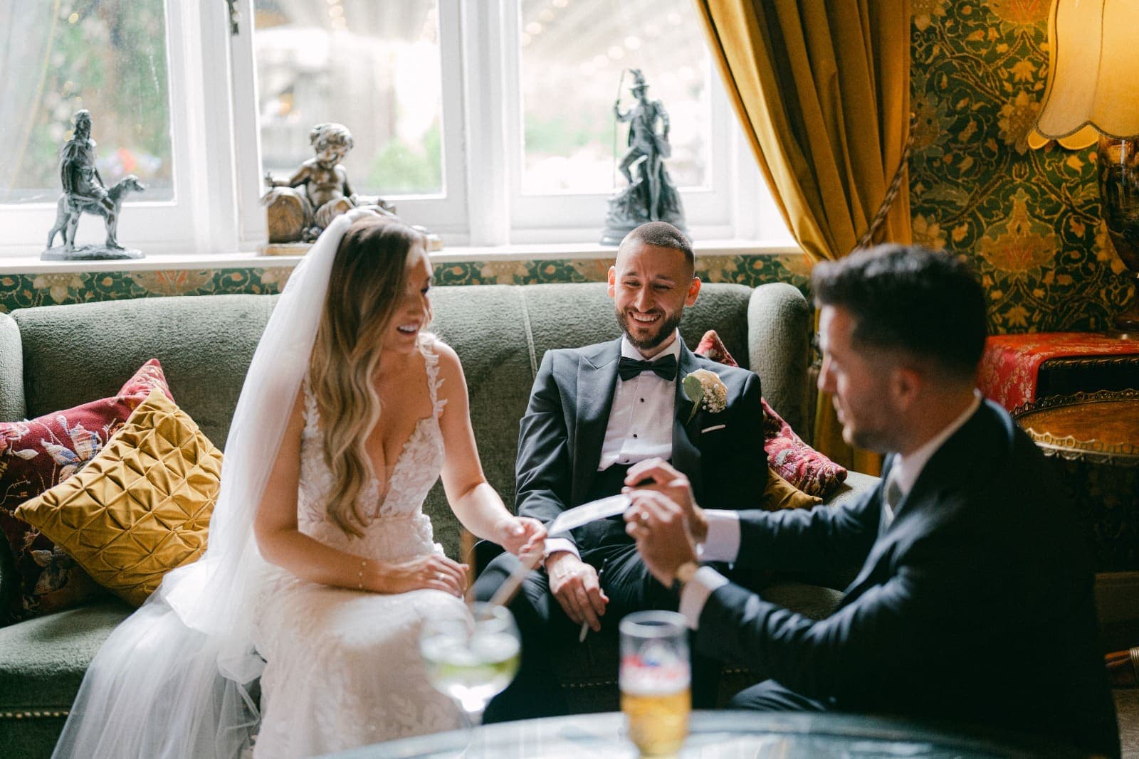 Amy and Luke laugh on the sofa as Jamie hands a card across the table