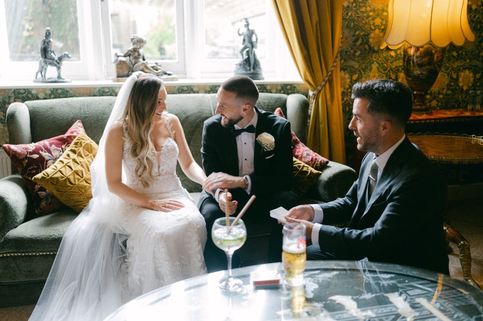 Amy and Luke smile at each other on the sofa as Jamie holds a set of cards