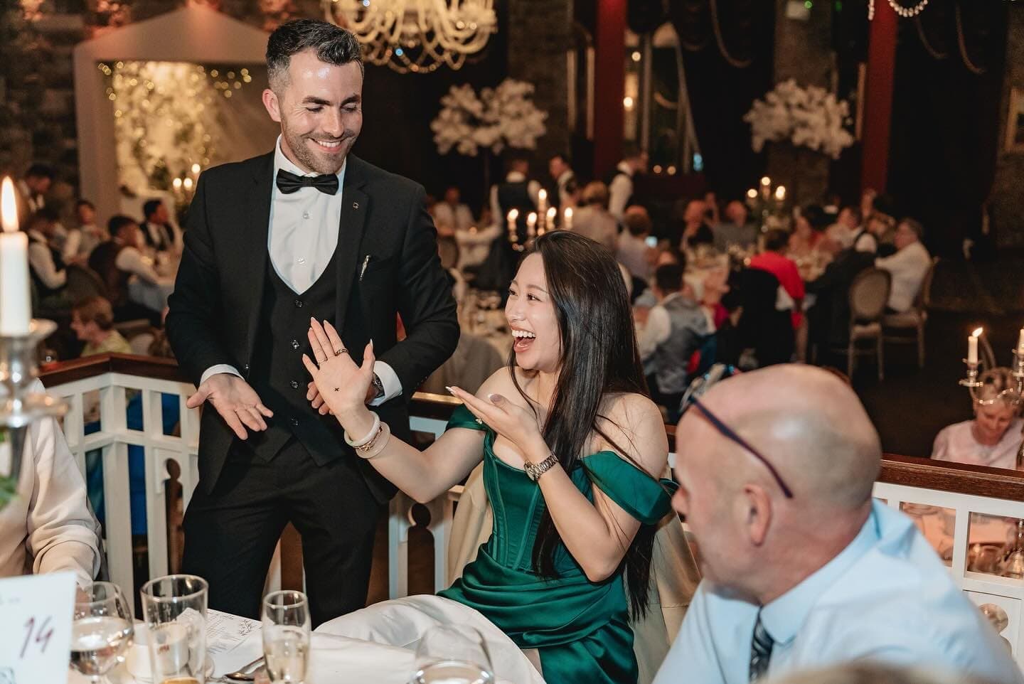 At Alex and Suzanne's wedding, the guest in green laughs and holds up her palm as Jamie smiles beside her