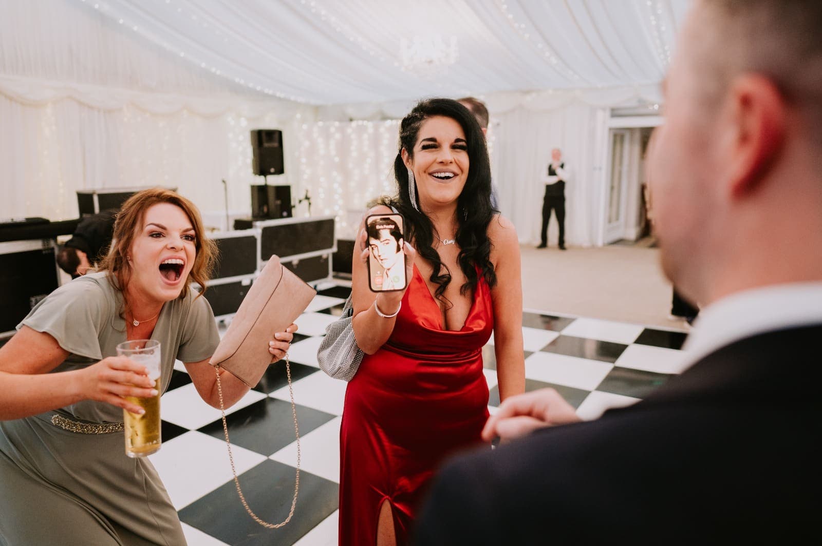 Two guests by the dance floor shriek with laughter at Jamie's trick, one holding up a phone