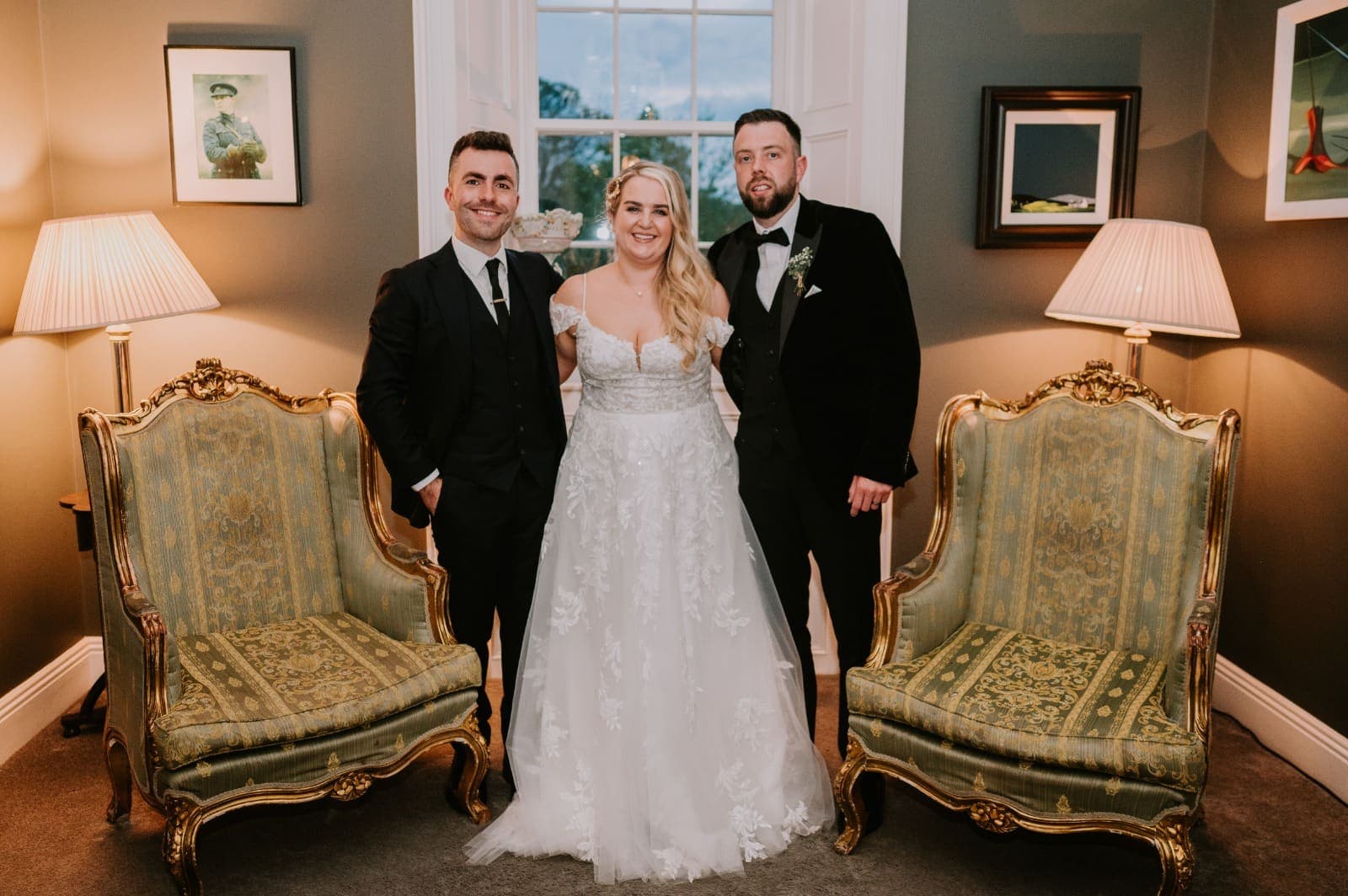 Jamie stands with Janice and Oisin between two gilt armchairs
