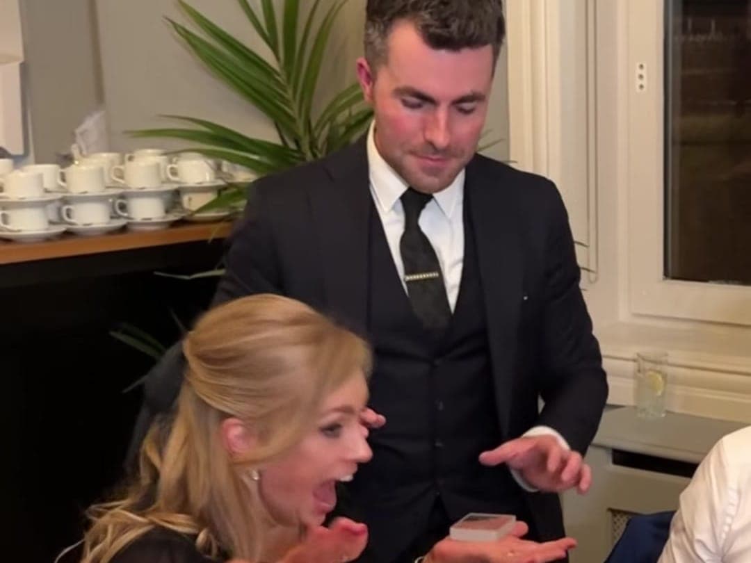 A wedding guest throws up her hands and gasps as Jamie holds out the cards at her dinner table