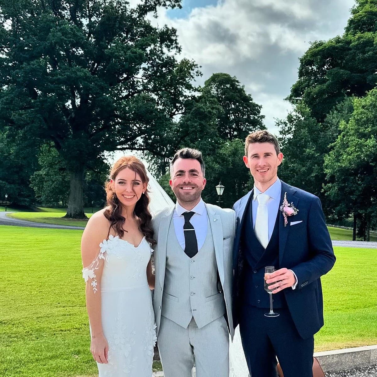 Jamie stands between Bronagh and Aaron on the sunny lawn at Tankardstown House, tall trees behind them