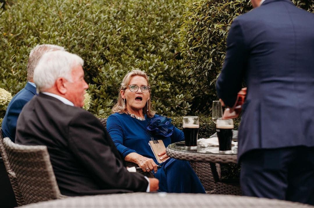 On the terrace at Tankardstown House, a guest in a blue dress gasps at a card trick during the drinks