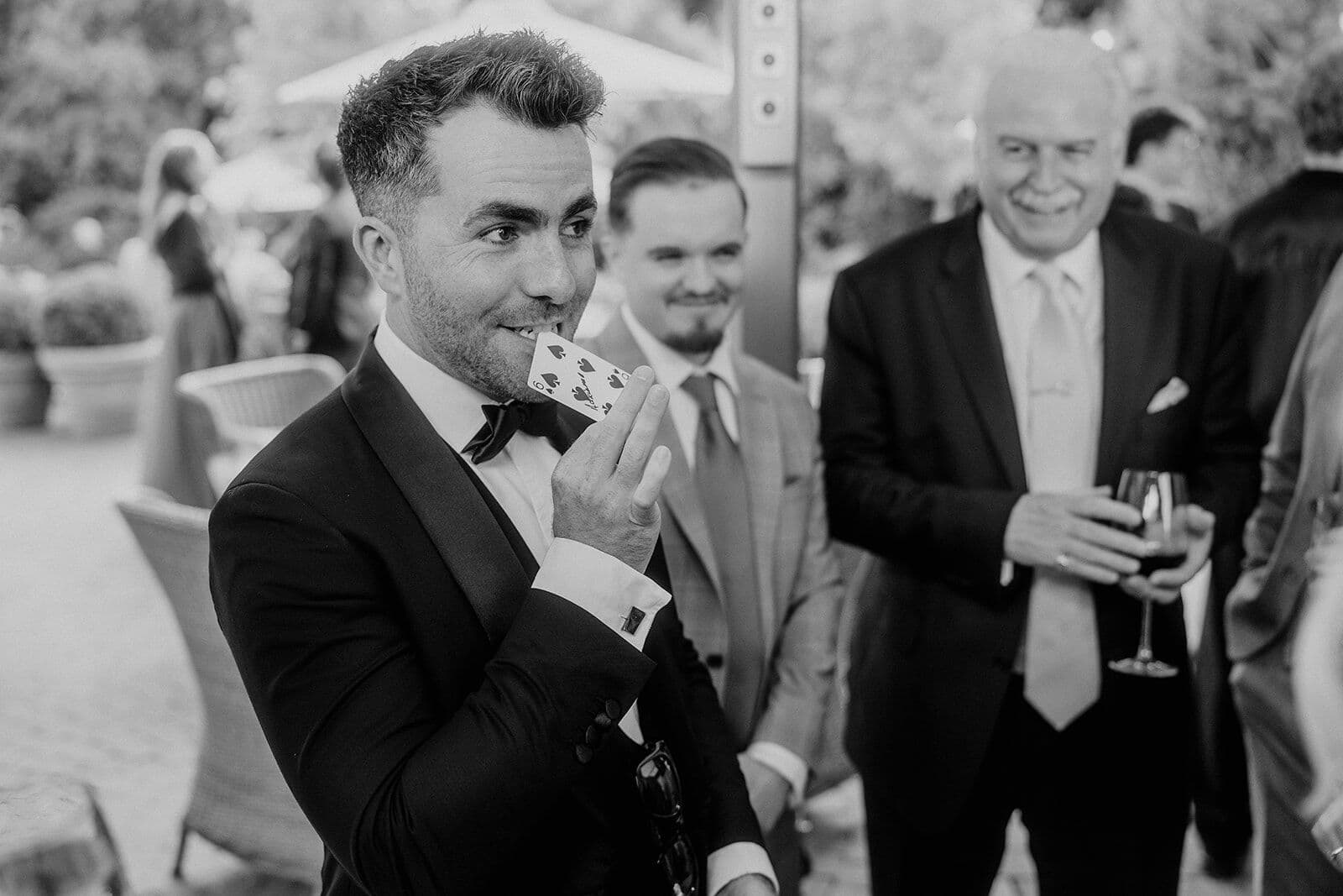 Black and white: Jamie holds a playing card in his teeth as guests smile in the garden