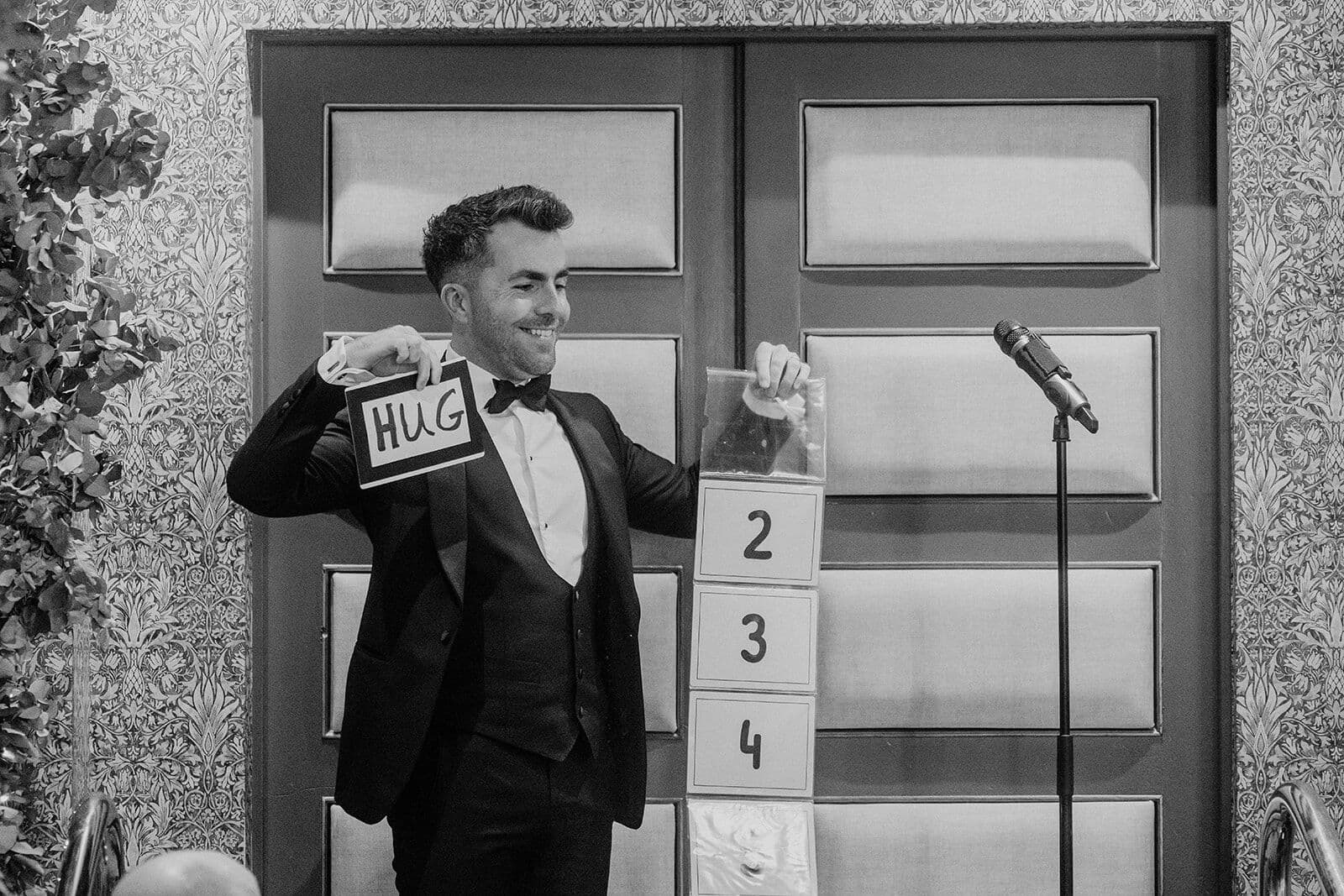 Black and white: Jamie holds up a card that reads HUG beside the numbered cards