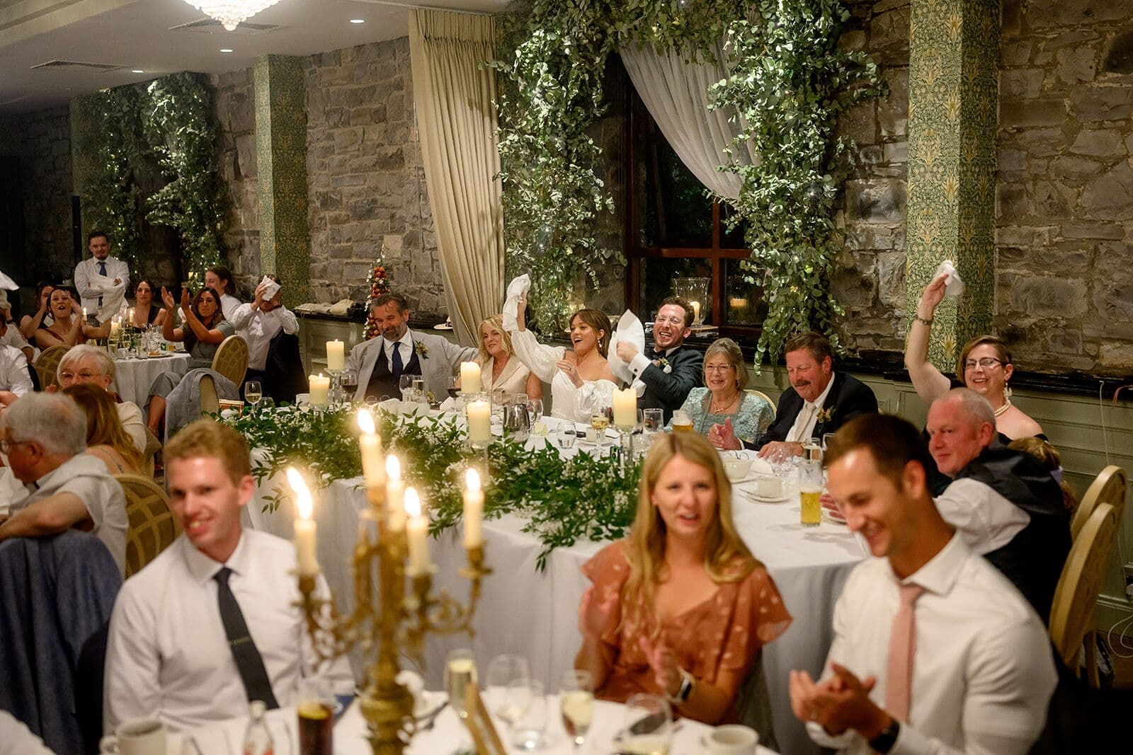 The whole room claps and waves napkins, the couple smiling at the top table